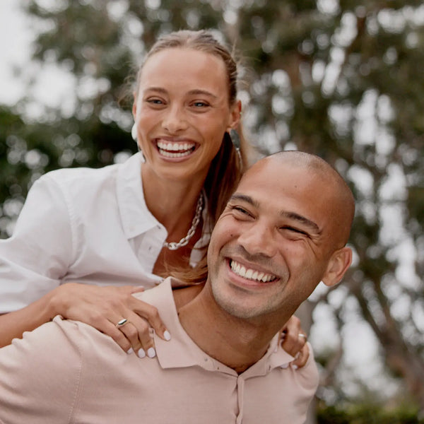 A happy couple outisde, smiling while the man holds the woman on his back